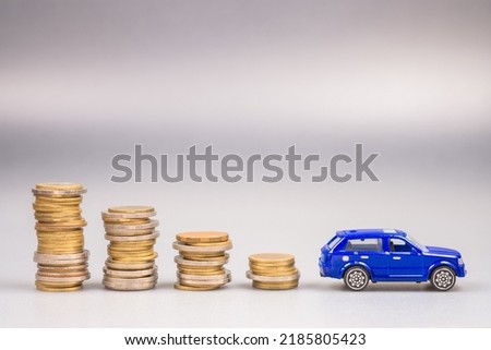 Lower stack money with a small blue car at the end, save the money for buying a new car, car and budget, finance and insurance, use money less about the car