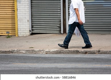 The Lower Torso Of A Man Walking Down The Sidewalk Along The Side Of The Road.