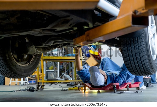 Lower view\
under car garage worker or technician lie down and check problem in\
workplace area. Garage management system support employee for\
working with happiness\
concept.