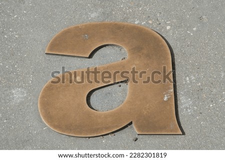 Lowercase letter a in bronze on the asphalt of a street