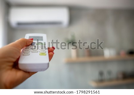 Lowering and Turning Off Air Conditioning to Conserve Eletricity Energy. Turn On the Air Conditioner. The girl's hand is using a remote control to turn on the air conditioning in the room