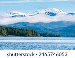 Low-hanging clouds over snow-capped mountains and evergreen forest along the Carroll Inlet near Ketchikan, Alaska