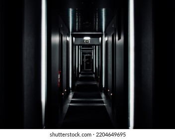 A low-key shot with a shallow depth of field of a black hotel corridor with a selective focus in the middle, with white vertical daylight lamps reflecting from the ceiling, an emergency exit sign - Shutterstock ID 2204649695