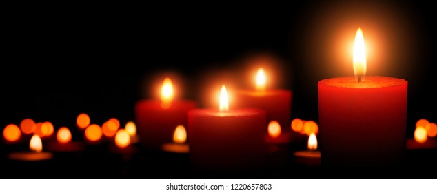 Low-key studio shot of elegant advent candles with four flames in the foreground, black background with defocused flames