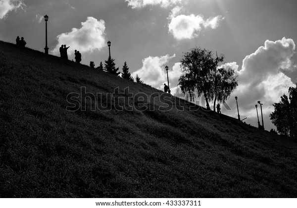 Low-key summer black and white park landscape\
with distant people\
silhouettes
