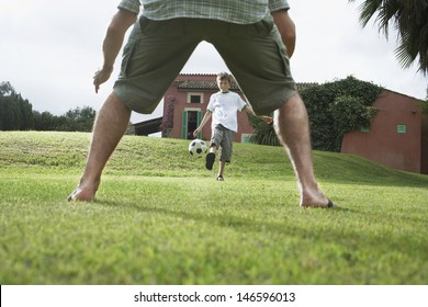 Lowsection Of Father With Son Playing Football In Backyard