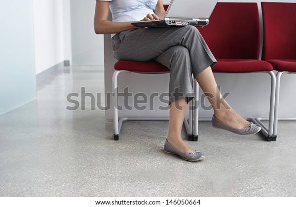 Lowsection of a female executive using laptop on\
chair in corridor