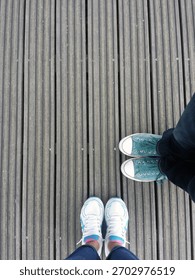 A low-section, personal perspective view of two people standing on a wooden footbridge