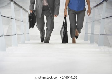 Lowsection of two businesspeople walking up stairs with bags in office
