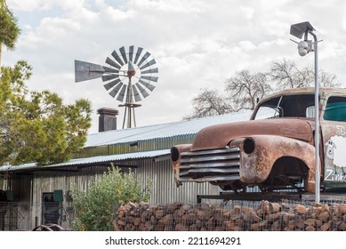 LOXTON, SOUTH AFRICA - SEP 2, 2022: A Street Scene, With A Corrugated Iron Building, Windmill And A Vintage Car Wreck, In Loxton In The Northern Cape Karoo. A Security Camera Is Visible