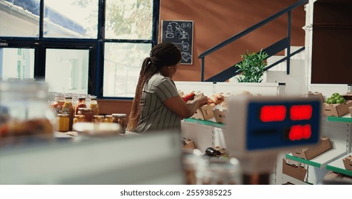 Loyal customer checking bio bulk products in zero waste shop, shopping for fresh natural groceries to restock pantry supplies. African american woman looks for vegan food. Handheld shot.