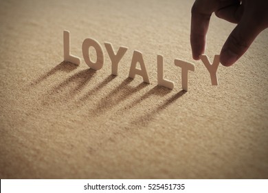 LOYALTY wood word on compressed board with human's finger at Y letter