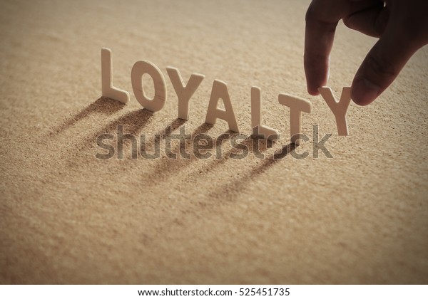 LOYALTY wood word on compressed board with human\'s\
finger at Y letter