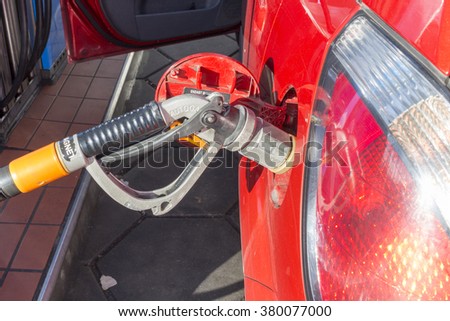 a LPG fuel pump nozzle at a red car with LPG terminal behind the original filler cap. When refueling exits cold gas and condenses on the air