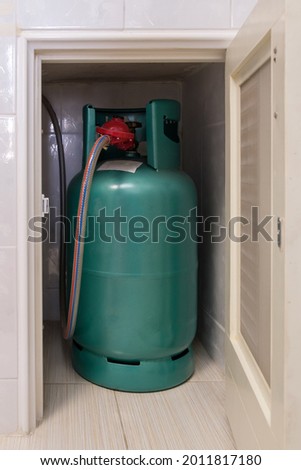 The LPG gas tank for cooking is stored in the small storage compartment near the gas stove bar in the kitchen, front view for the copy space.