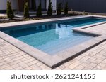 L-shaped pool is finished with a gray border stone. Clean blue water in the pool. Steps for a smooth descent into the water. Relaxing in the backyard of a country house