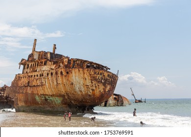 Luanda / Angola - 06/11/2018: View Of A Abandoned Ships Carcasses In The Ships Cemetery, Children Bathing On The Beach