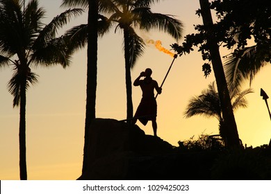 luau on Maui at sunset with silhouette of  man blowing conch shell and holding a fire torch among the palm trees