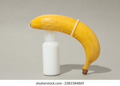 Lubricant with a banana in a condom, on a gray background.