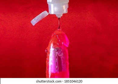Lubricant for sex drips on a vibrator on a red background with a place copyspace text for a sex shop. Dildo for adults