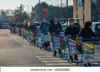 Lucca, Tuscany, Italy 03/21/20 - Line Of Italian Men And Women With Coronavirus Protective Masks Waiting With Shopping Carts To Do Grocery. National Lockdown, Anxious And Stressed People Fear Shortage