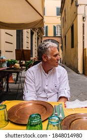 Lucca, Tuscany, Italy - 05/08/2020: Man Sitting In A Traditional Italian Restaurant And Waiting For His Lunch. Traditional Tuscan And Italian Background. Real Life Moment