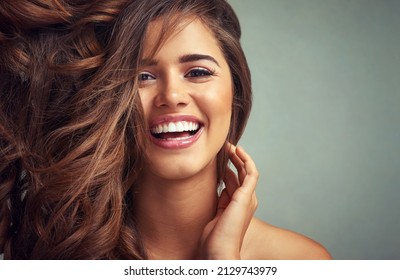 Lucious locks and happy laughter. Studio portrait of a beautiful woman with long locks posing against a grey background.
