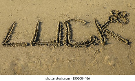 Luck Word With Four Leaf Clover Written In Sand On Wet Sandy Beach. New Beginnings, Expexctation, Hope. Copy Space For Ad Banner.