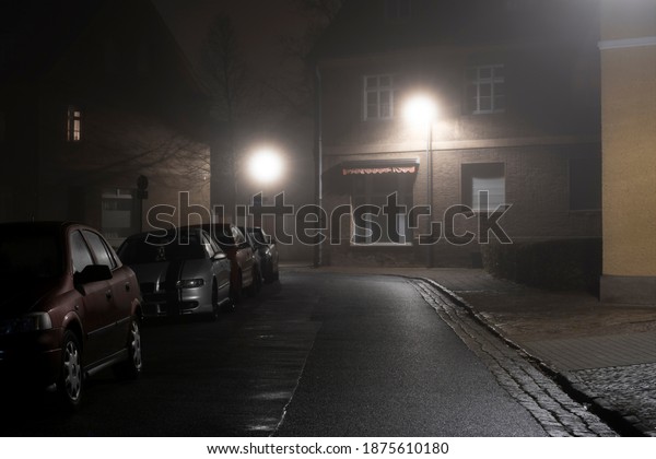 Luckenwalde , Germany , 14.12.2020 , Fog at\
night in the streets of Luckenwalde,cars parked on the side of the\
road in the light of street\
lights