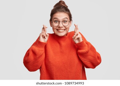 Lucky beautiful Caucasian female crosses fingers , hopes all wishes come true, wears oversized red sweater and spectacles, isolated over white background. People, body language and happiness - Shutterstock ID 1089734993