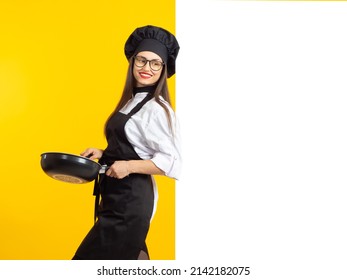 Una hermosa y afortunada cocinera. Retrato de una joven chef y un lugar para el texto. Una alegre chica con una sartén. El cocinero está parado de lado y sonriendo. El concepto de cafés y restaurantes.