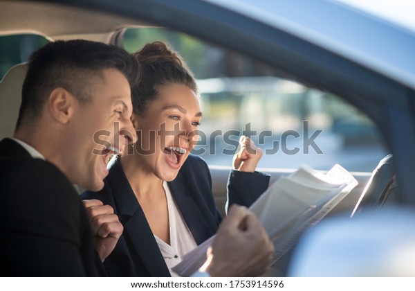 Lucky day. Successful young man\
and woman with open mouths raised fists, delighted, sitting in\
car