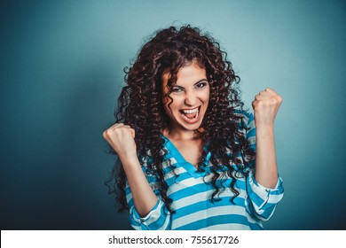 Lucky girl. Closeup portrait happy young brunette curly woman happy exults pumping fists ecstatic isolated blue background. Celebrate success concept. Human facial expression emotions body language