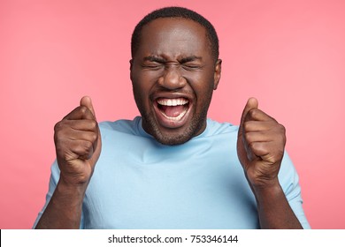 Lucky happy overjoyed male winner clenches fists, rejoices triumph at work, glad to recieve high profits, has own prosperous business. Attractive African American man achieves goals