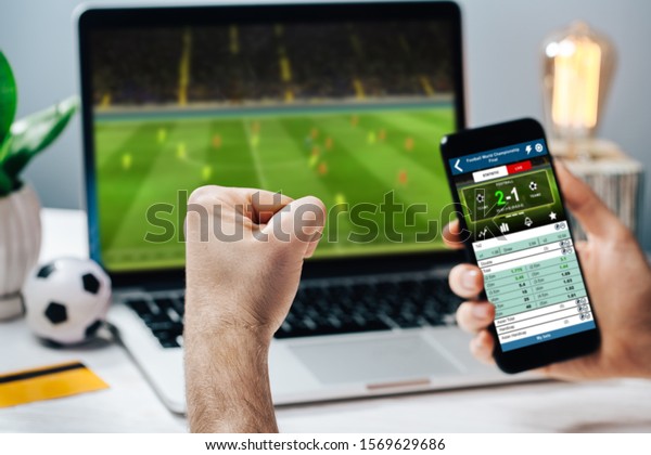 Lucky man celebrating money\
win. Male fan watching football play online broadcast on his\
laptop, cheering for his favorite team and making bets at\
bookmaker\'s website.