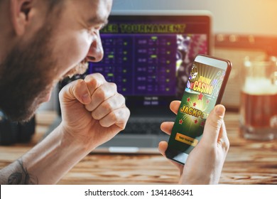 Lucky Man Celebrating Victory After Getting Jackpot In Online Casino. Poker Tournament On The Laptop Screen On The Background.