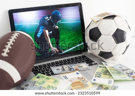 Lucky man celebrating victory after making bets using gambling mobile application on his phone. Football match online broadcast on laptop screen on the background.