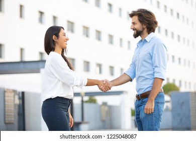 Lucky multicultural partners shaking hands on meeting in city. Professional multiethnic businesspeople near office building, side view. Teamwork concept