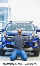 Lucky owner. Vertical full length shot of an excited young African man screaming happily with his arms raised standing on his knees near his new car at the car dealership winner winning luck offer