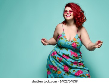 Lucky plus-size lady overweight woman in fashion sunglasses and colorful sundress happy dancing, celebrating on mint background with free text space