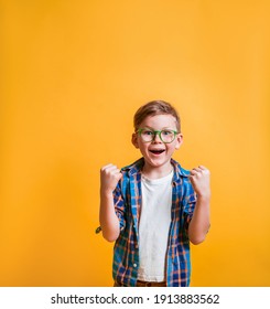Glücklicher Schuljunge in Brille einzeln auf gelbem Hintergrund. Sehr glücklicher und aufgeregter Junge, der eine Gewinnergeste mit aufgeweckten Armen, Lächeln und Schreien für den Erfolg macht. Feiern. Boy Superheld