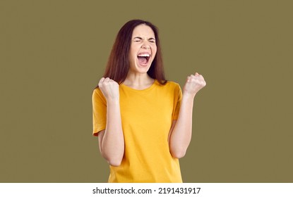 Lucky Young Woman Achieves Her Goal, Wins Lots Of Money Or Inherits Huge Fortune. Happy Excited Crazy Girl In T Shirt Isolated On Solid Brown Background Fist Pumping And Screaming YES I DID IT