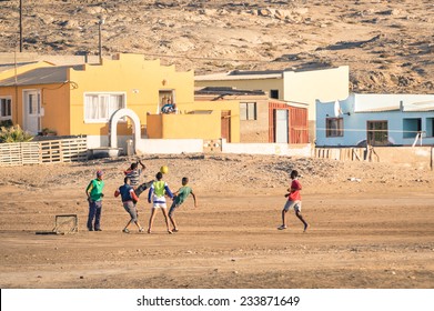 LUDERITZ, NAMIBIA - 24 NOVEMBER 2014: Local Young People Playing Football In The Playground Next To A Modern Township; For Lucky And Talented Players, Soccer Is A Fast Way To Escape Poverty Of Slums