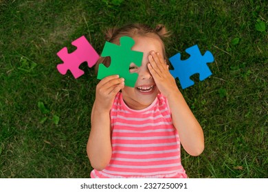 A ludicrous child is playing with puzzles while lying on the lawn grass. Children's toys for the development of logic and thinking