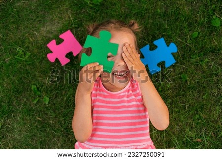 A ludicrous child is playing with puzzles while lying on the lawn grass. Children's toys for the development of logic and thinking