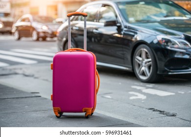 Luggage bag on the city street ready to pick by airport transfer taxi car. - Shutterstock ID 596931461