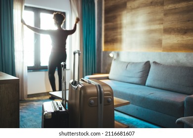 Luggage in modern hotel room with happy young adult female relaxing nearly window, African woman tourist looking to beautiful nature view. Time to travel, relaxation, journey, trip and vacation 
