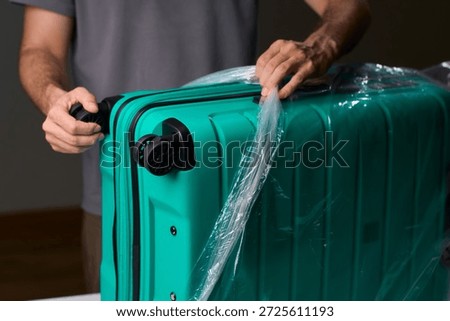 Luggage wrapping process, Worker securing suitcase with protective plastic film, Ensuring safety and protection through meticulous wrapping of belongings for travel
