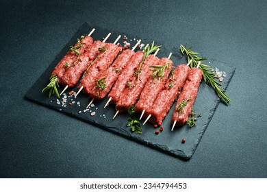 Lula kebab on skewers with spices in a black slate board on a stone background. Top view.