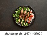 Lula kebab on wooden skewers served with fresh vegetables on black plate on dark background. Top view, flat lay, closeup